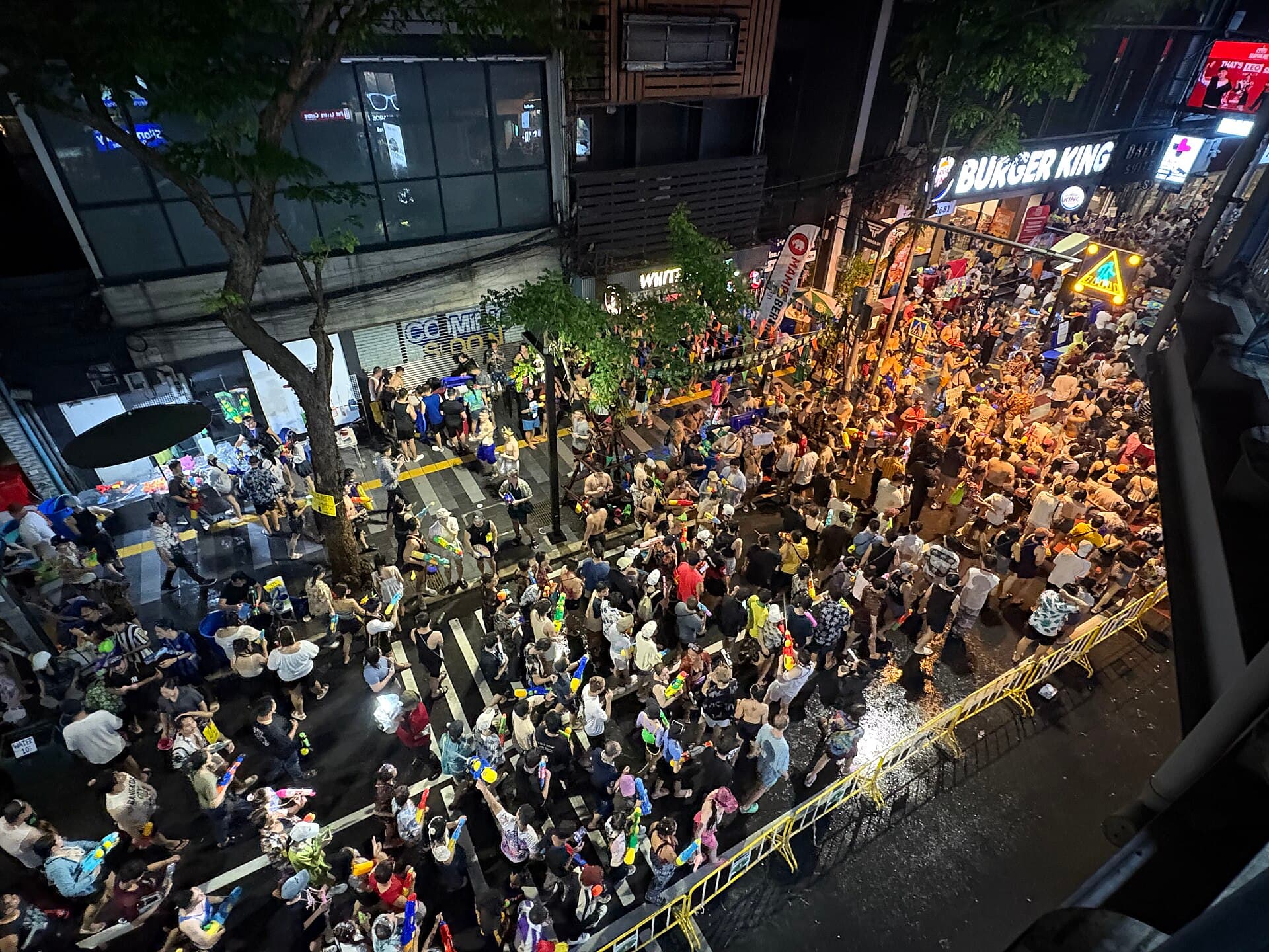 Crowd under the BTS Siam station tracks during Songkran, many holding phones in waterproof pouches