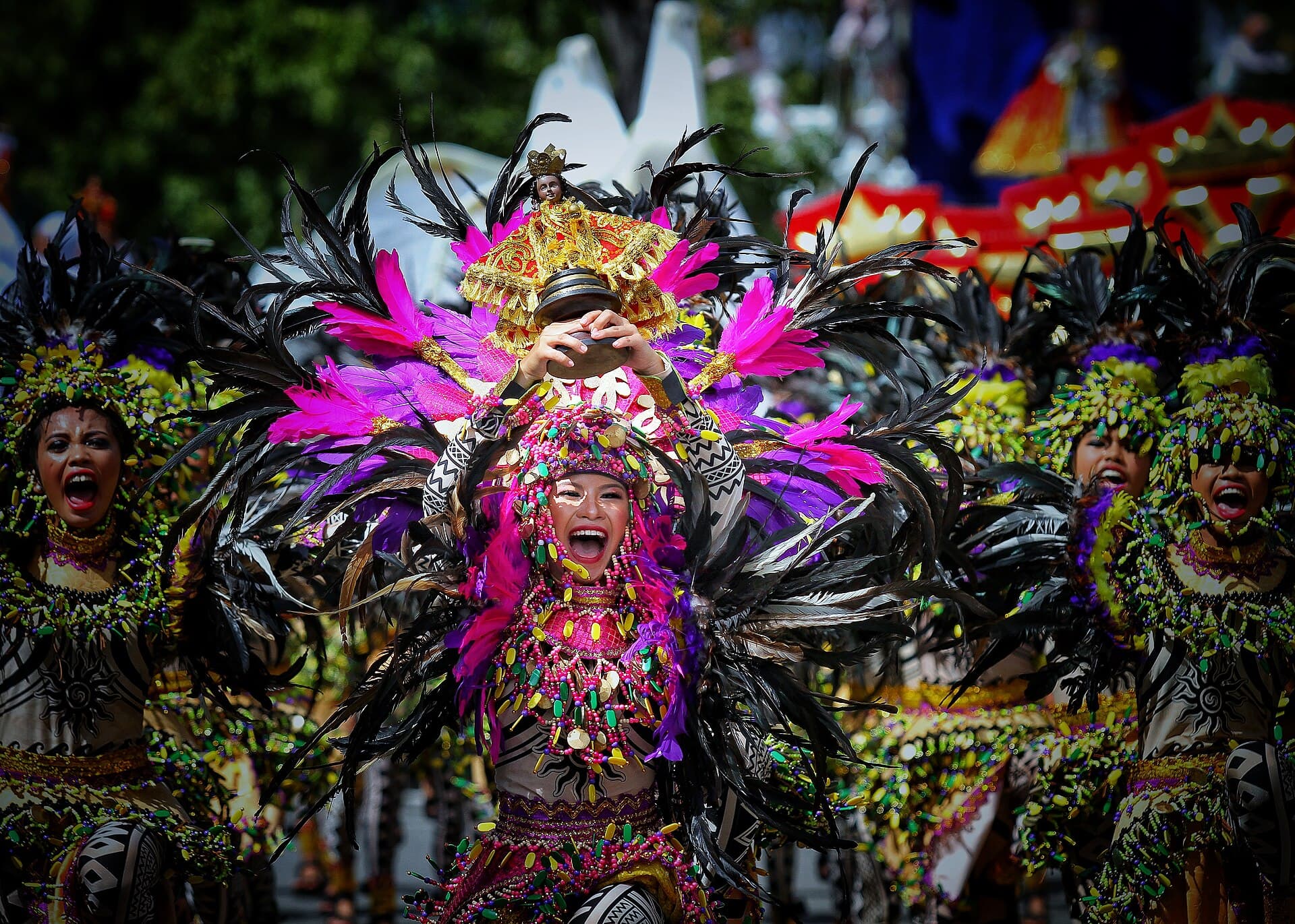 Sinulog street dancers in feathered costumes raising Santo Niño replicas on Osmeña Boulevard, Cebu City