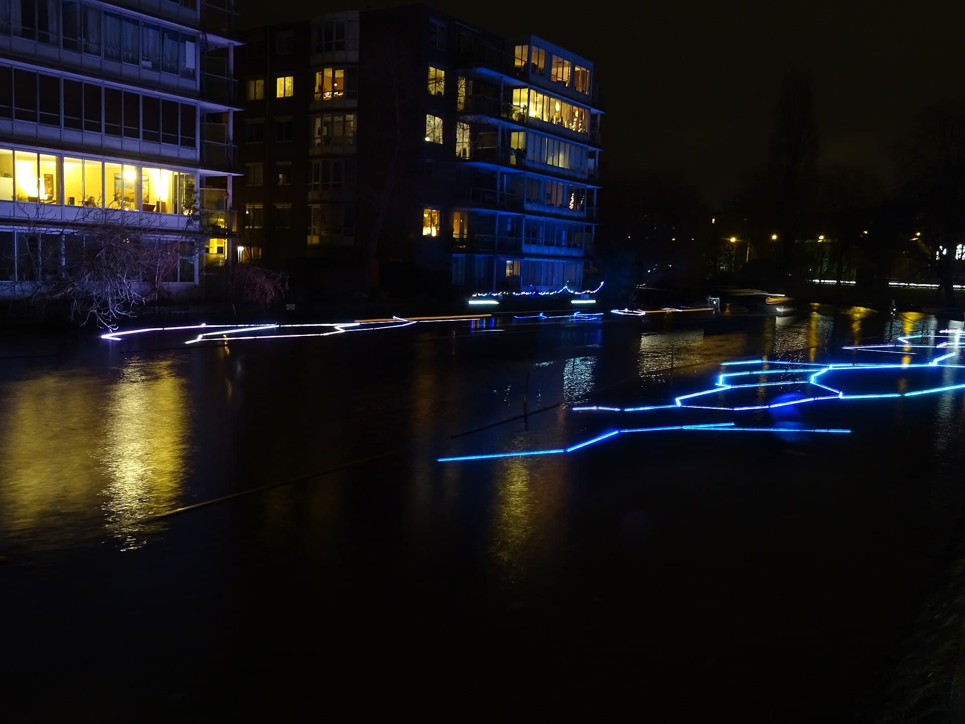 A heated canal cruise boat with lit windows passing under a stone bridge at night