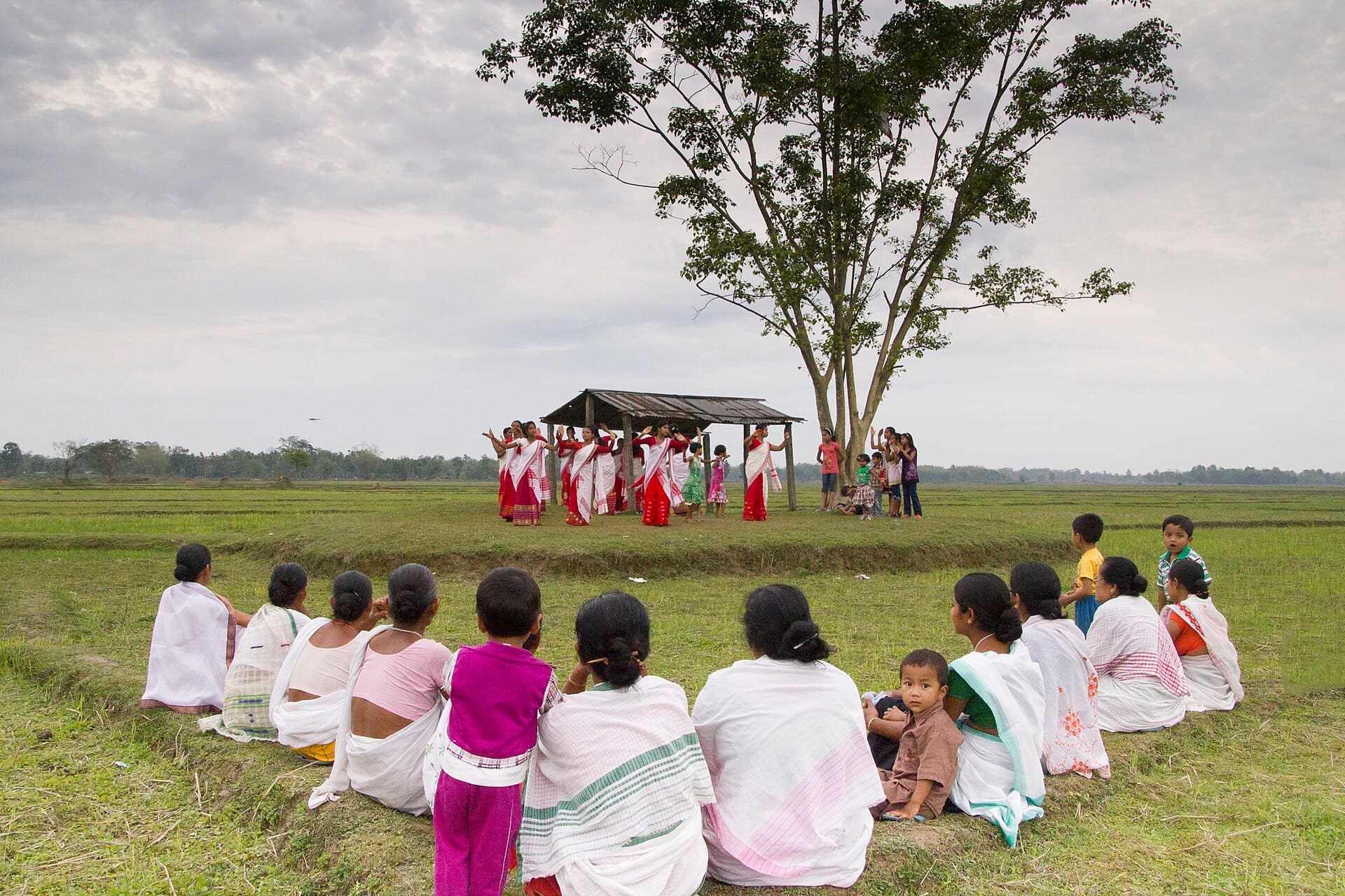 Young Bihu dancers in red and white mekhela chador and dhuti performing on a stage