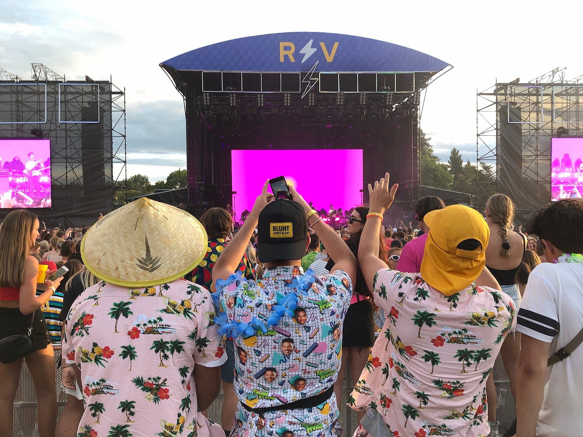 Wide view of the Rhythm and Vines main stage crowd at Waiohika Estate at sunset, with the vineyard slope and hills behind