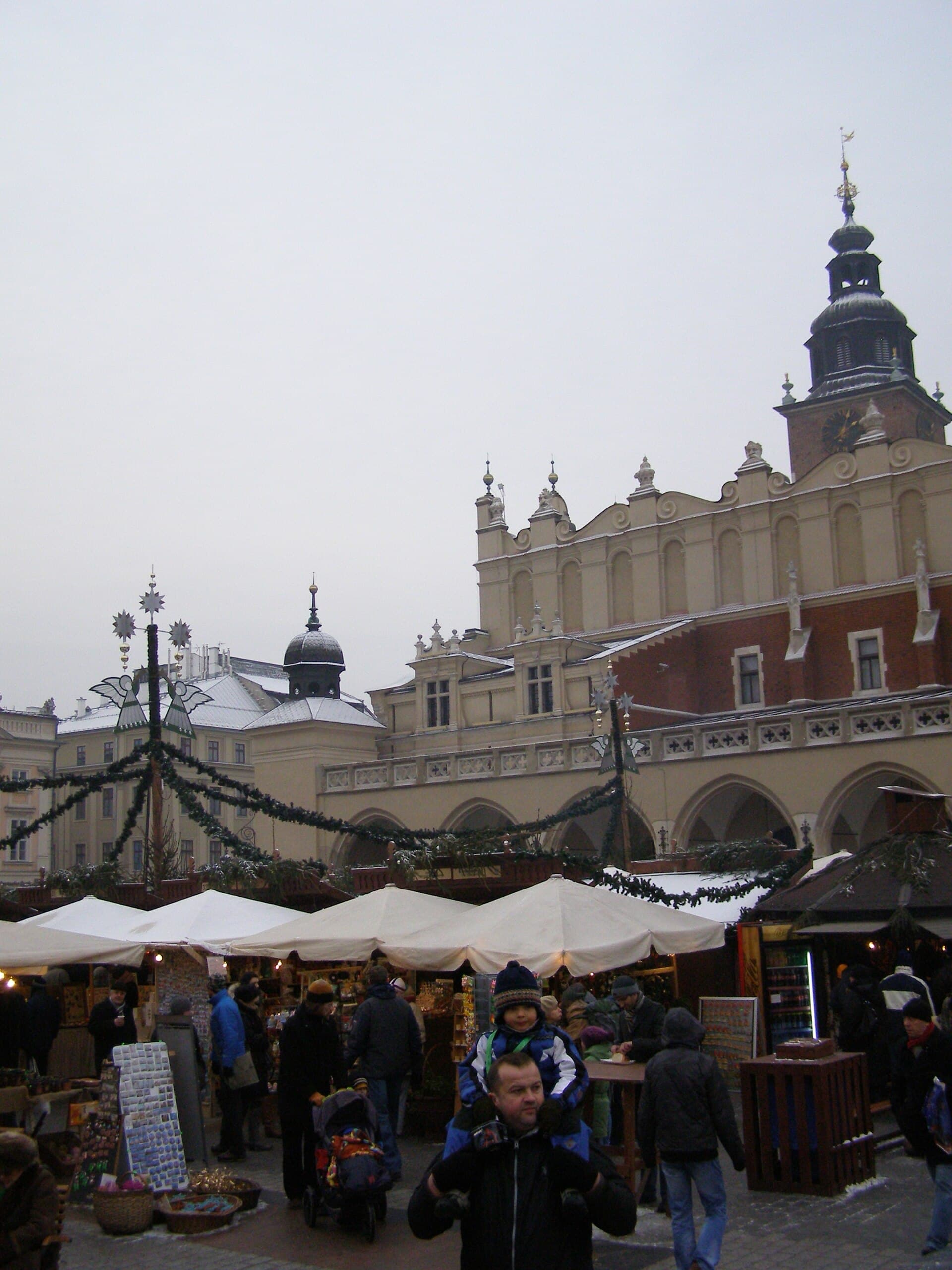 The Rynek Glowny under snow with people in winter coats walking between stalls