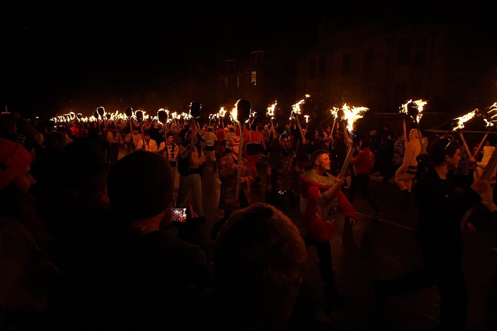 Up Helly Aa torchlit procession of guizers on the Lerwick Hillhead at night, wide shot with the galley