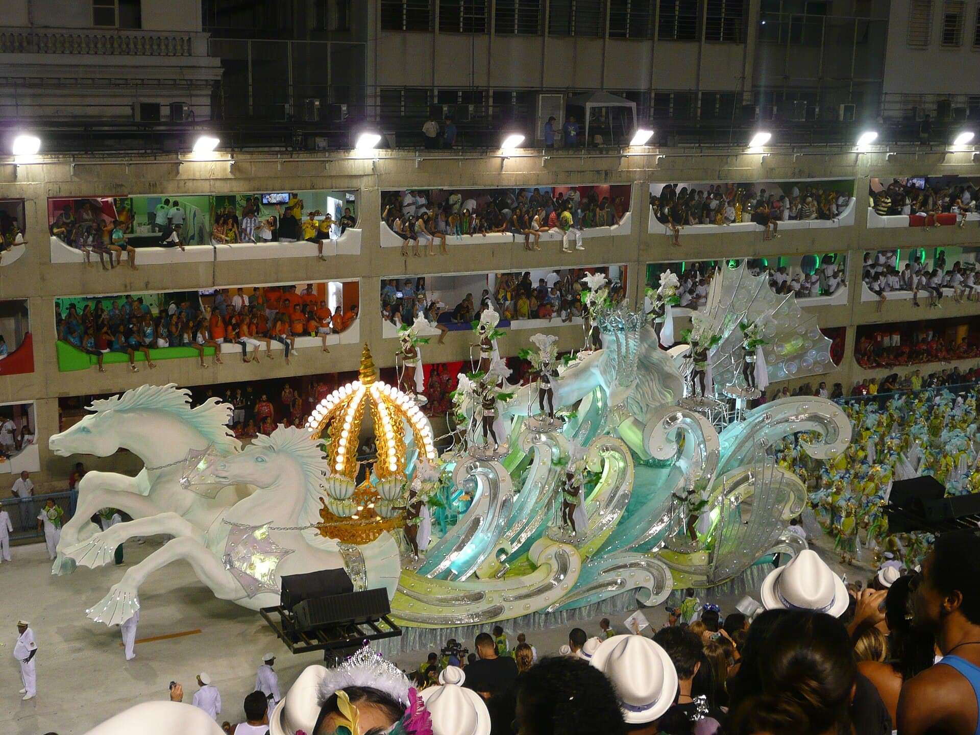 Wide shot of the Sambadrome at night with a samba school on the avenue and full grandstands
