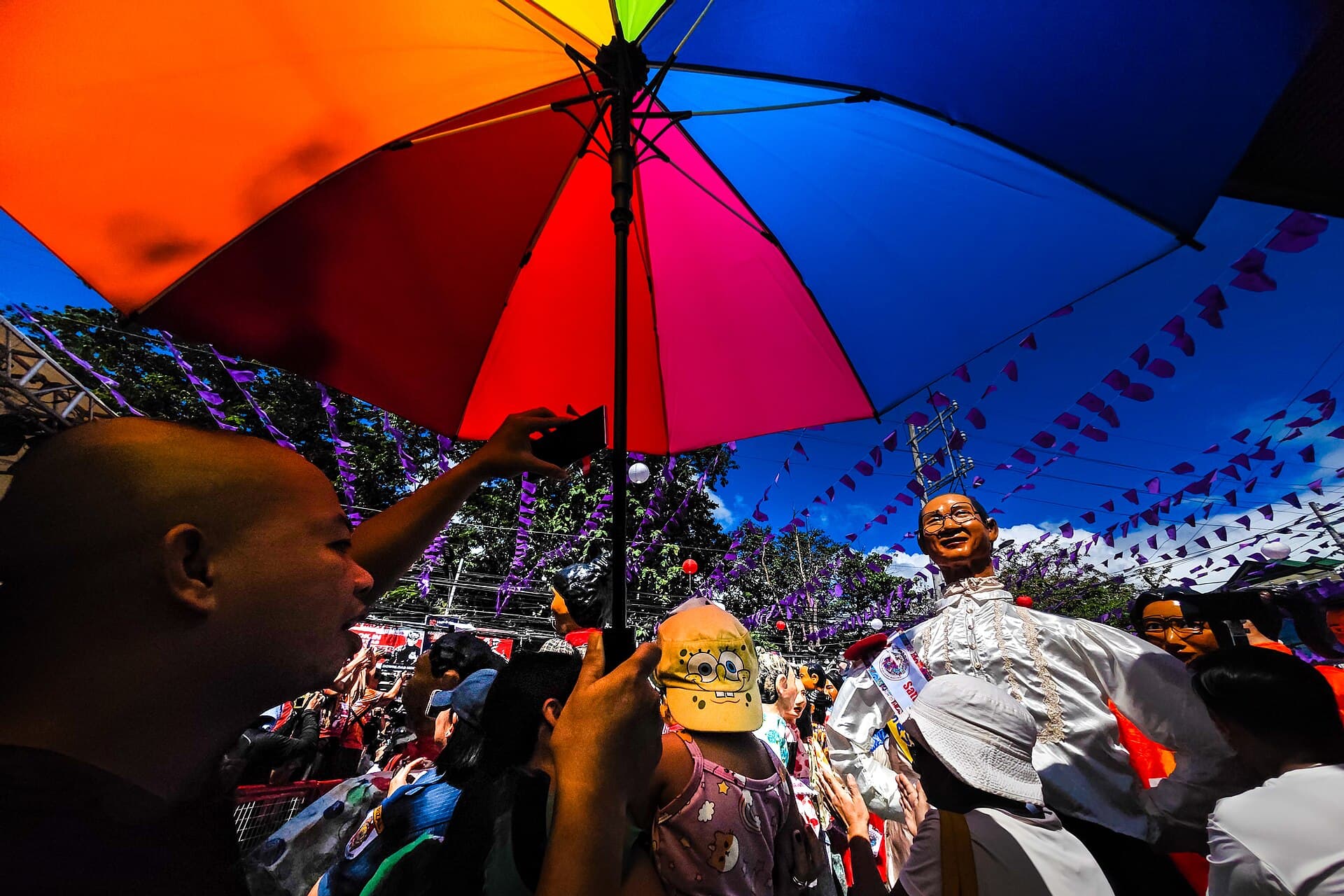 Wide shot of a parade of papier-mâché higantes on M.L. Quezon Avenue in Poblacion, Angono, Rizal