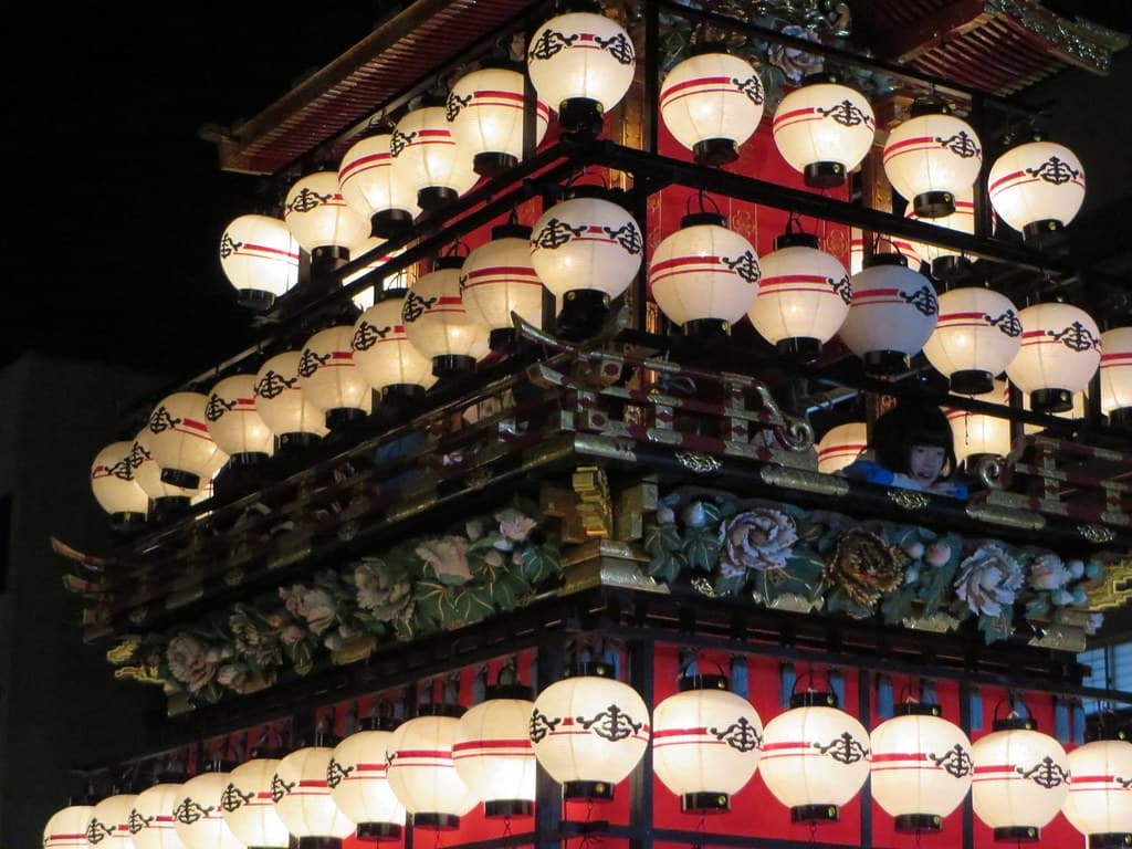 A crowd with phones held up photographing a lantern-lit float at night
