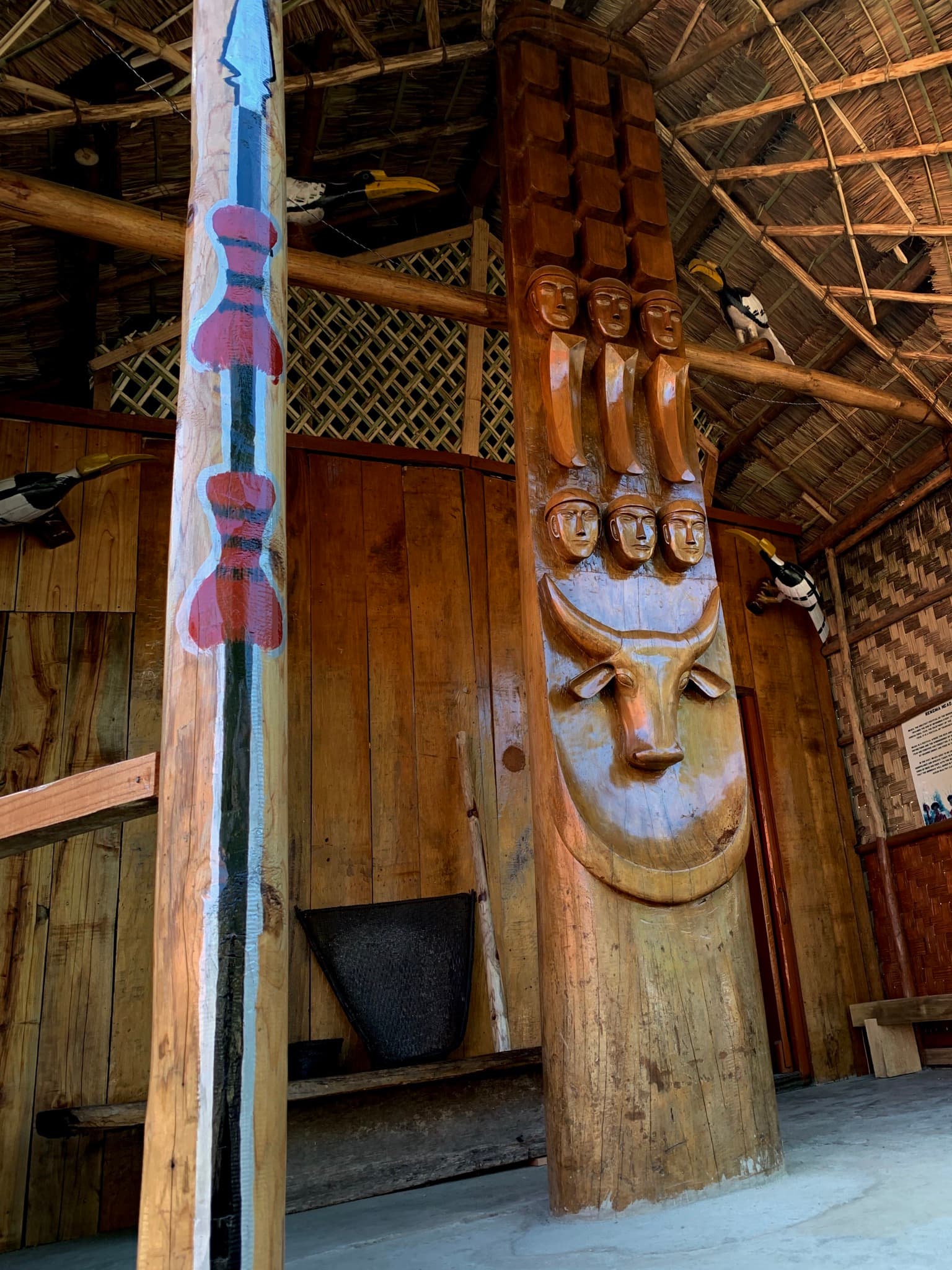 A traditional Naga morung with carved horns on the roof beam and a log drum beside it
