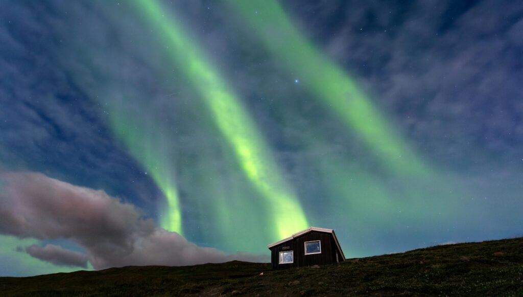 Cozy wooden house beneath vibrant Northern Lights with snowy landscape in a remote Arctic setting