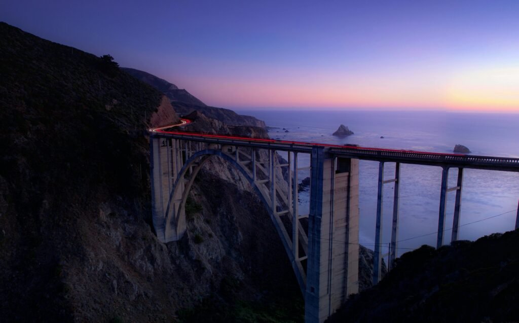 Sunset view of Bixby Bridge along the Pacific Coast Highway in California, with golden light illuminating the cliffs and ocean below