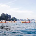 Person kayaking through the emerald waters of Ha Long Bay, surrounded by towering limestone karsts