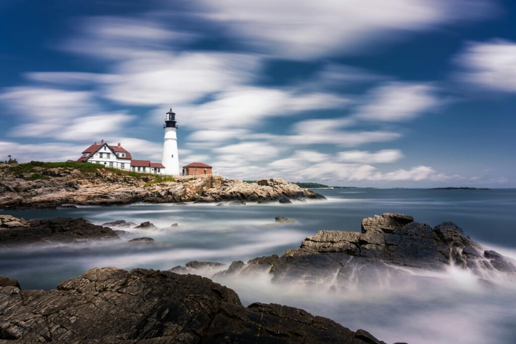 Scenic view of Portland Head Light lighthouse on a rocky Maine coastline with dramatic clouds and smooth ocean waves captured in long exposure