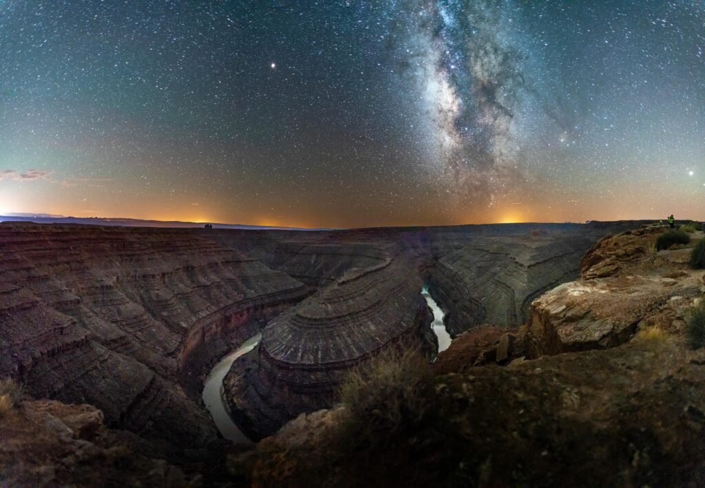 Milky Way galaxy shining brightly over the winding Goosenecks of the San Juan River in Utah, with dramatic canyon cliffs under a starry night sky.
