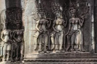 Ancient stone wall carvings and tree roots entwined in the temple ruins of Ta Prohm, Angkor, Cambodia, showcasing iconic Khmer architecture.