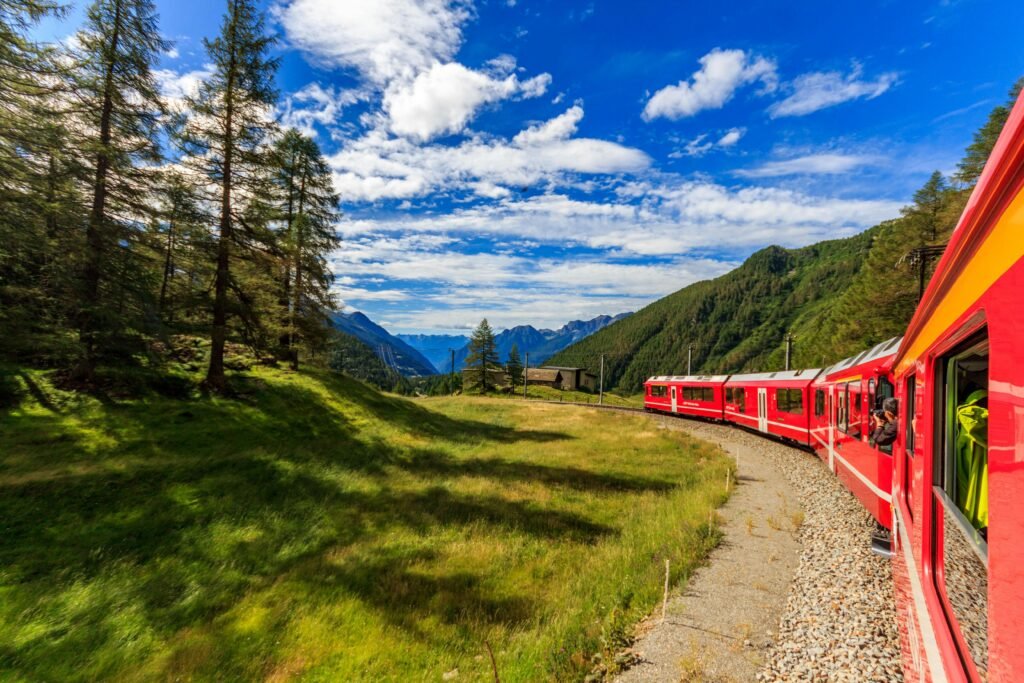 Scenic train traveling through the Swiss Alps with snow-capped mountains, green valleys, and clear blue skies in the background