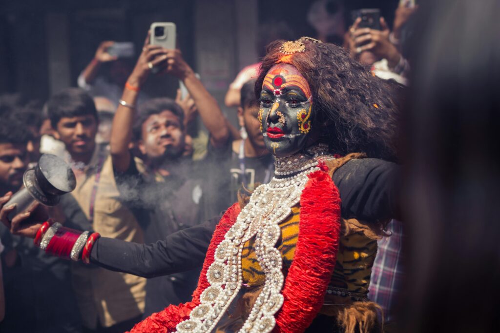 Traditional street performer dressed as Goddess Kali during a cultural festival in Varanasi, India with onlookers capturing the moment