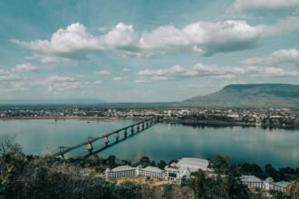 Scenic view of the Mekong River and bridge in Pakse, Laos, with the city skyline and Phou Salao mountain in the background under a partly cloudy sky